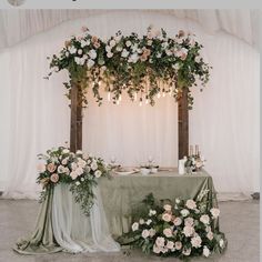 the table is set up with flowers and greenery for an outdoor wedding reception in front of a white backdrop