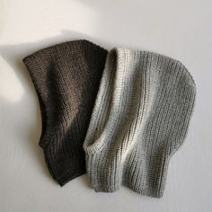 two knitted hats sitting next to each other on top of a white tablecloth