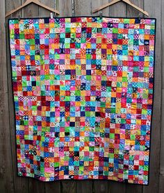 a multicolored quilt hanging on a wooden fence with clothes pins attached to it