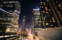 the city skyline is lit up at night with skyscrapers in the foreground and street lights on either side