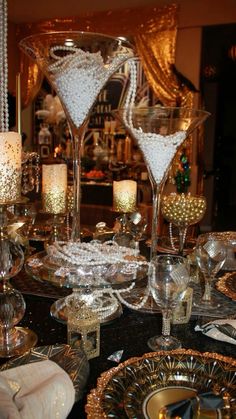 a table topped with lots of glasses filled with white and gold confetti next to candles