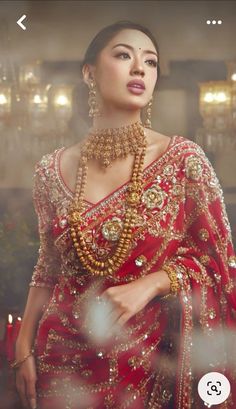 a woman in a red and gold sari with jewelry on her neck is looking into the distance