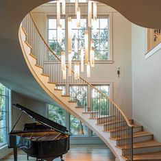 a grand piano sitting under a chandelier in a living room next to a staircase