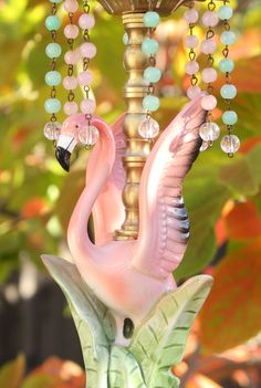 a pink flamingo lamp with beads hanging from it's side in front of some leaves