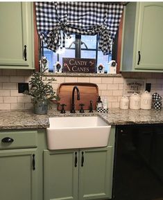 a kitchen with green cabinets, black and white checkered window valance, and an old fashioned farmhouse sink