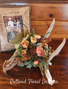 an arrangement of flowers and antler horns on a table next to a framed photo