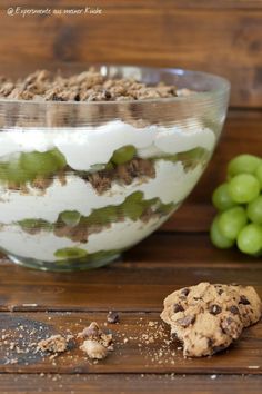 a glass bowl filled with food next to grapes and a cookie on a wooden table