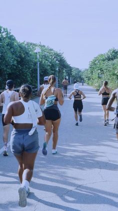 a group of people running down a street next to trees and bushes on either side of the road