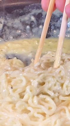 someone holding chopsticks over noodles in a bowl