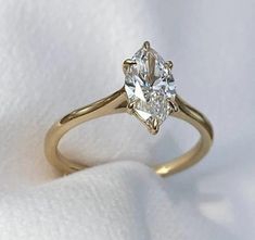 a yellow gold ring with an oval cut diamond in the center on a white cloth