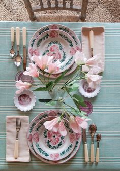 the table is set with plates, silverware and pink flowers in vases on them