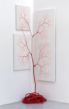 two paintings on the wall behind a red wire tree with branches in front of it