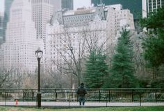 a man walking across a lush green park next to tall buildings in a cityscape