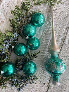 green glass ornaments are arranged on a white wooden surface with greenery and blue berries