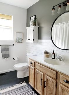 a bathroom with white tile and wood cabinetry is shown in this image, there's a round mirror above the sink