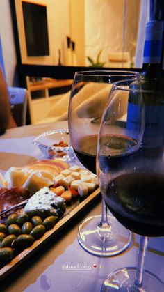 two glasses of wine sitting on top of a table next to cheese and crackers