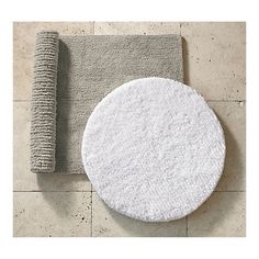 a round white rug sitting on top of a bathroom floor next to a gray towel