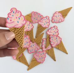 a hand holding some pink and gold ice cream cones with sprinkles on them