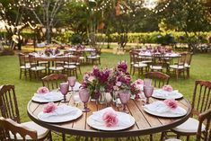 a wooden table topped with white plates and pink flowers