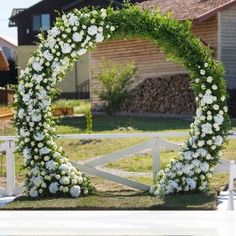 a wedding arch decorated with white flowers and greenery in front of a wooden barn