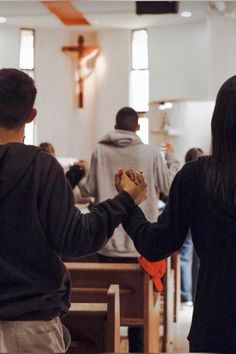 two people holding hands while standing in front of pews with other people behind them