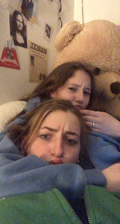 two women laying in bed with a teddy bear on the wall behind them and one woman covering her face