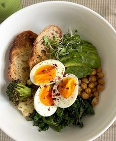 a white bowl filled with eggs, beans and broccoli on top of a table