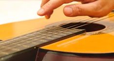 a person playing an acoustic guitar with their hand on the fretboard and fingers pointing at it