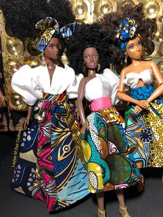 two barbie dolls standing next to each other in front of a gold wall with african designs on it