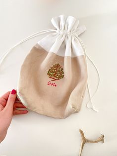 a hand holding a drawstring bag with a small tree on the front and side