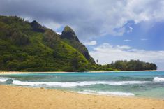 a beach with waves crashing on the sand and green mountains in the backgroud