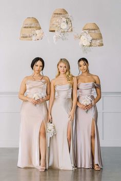 three bridesmaids posing for a photo in their dresses with flowers hanging from the ceiling