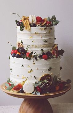 a three tiered cake with fruit and leaves on the top is sitting on a wooden stand