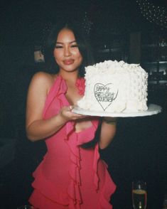 a woman in a pink dress holding up a white cake with hearts on the top