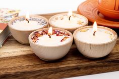 four white candles sitting on top of a wooden tray