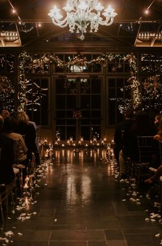 a room filled with lots of people sitting in front of a chandelier and windows