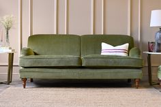 a green couch sitting on top of a rug next to a table with flowers in vases