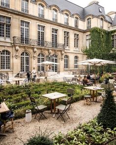 an outdoor garden with tables and chairs in front of a large building