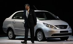 a man in a suit standing next to a silver car on a dark stage area