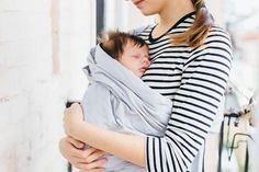 a woman holding a baby wrapped in a grey and black wrap on her chest,