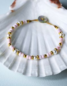 a pink and gold beaded bracelet on top of a seashell with a shell in the background