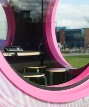 there is a pink and black circular mirror in front of some tables with laptops on them