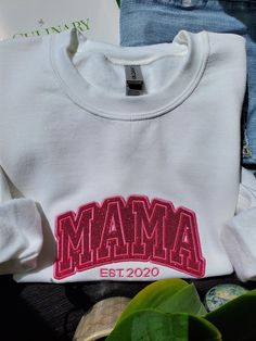 Sparkle like a Mama! Get ready to shine with our dazzling Unisex Glitter Embroidered Mama Sweatshirt! This cozy sweatshirt is not just for Mom's - it's for anyone who wants to add little sparkle to their wardrobe! The glittery "Mama" embroidery is the perfect touch of glamour and fun. Whether you're a proud parent, a cool aunt, or just someone who loves a little bit of bling, this sweatshirt is for you! ➡️Sweatshirts are Unisex Fit PRODUCT DETAILS ✦ Sweatshirts are Unisex Gildan Heavy Blend G180 ✦ 50% USA Cotton, 50% Polyester 13.3 oz./lin.yd. ✦ Pill-resistant air jet yarn ✦ Double needle stitching throughout ✦ Set in sleeves ✦ 1x1 ribbed collar, cuffs and waistband with spandex SHIPPING All orders are shipped with tracking within 1-3 business days via Canada Post from Ontario, Canada. CAR Varsity Style Top With Embroidered Text For Winter, College Red Tops With Embroidered Text, Red College Tops With Embroidered Text, Red Embroidered Text College Tops, Pink Embroidered Tops For College, Red College Top With Embroidered Text, White Winter Top With Embroidered Text, White Embroidered Text Top For Winter, Winter Varsity Tops With Custom Embroidery