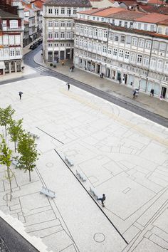 an aerial view of a city square with benches and trees in the foreground, surrounded by buildings