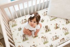 a baby sitting in a crib next to a pillow and blanket with animals on it