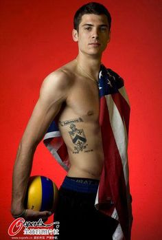 a shirtless man holding a beach ball and an american flag on his chest, standing in front of a red background