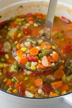 a ladle full of vegetable soup with carrots, peas and other veggies