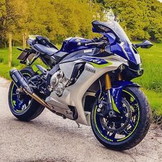 a blue and silver motorcycle parked on the side of a road next to a lush green field