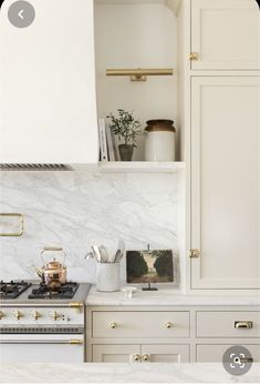 a kitchen with white cabinets and marble counter tops, gold pulls on the oven hood