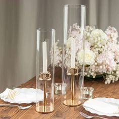 two tall glass candlesticks sitting on top of a wooden table next to flowers